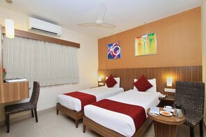 A hotel room with two beds, a desk, a chair, and a small table with a coffee pot. - La Sara Comforts (Bengaluru)