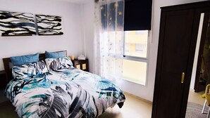 Ein Schlafzimmer mit Bett, Fenster mit Vorhang, Tür und Wand mit abstrakter Kunst.
