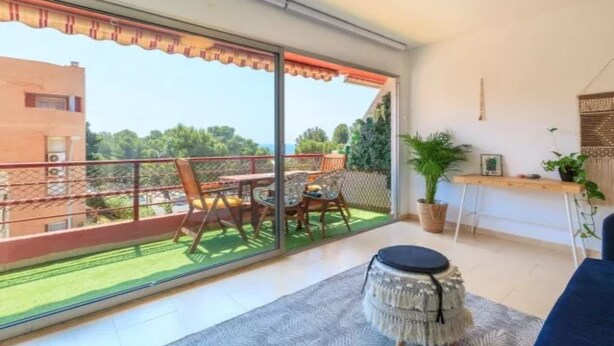 Ein Balkon mit Tisch und Stühlen, einem Blumentopf und Blick auf Grünflächen und Gebäude.