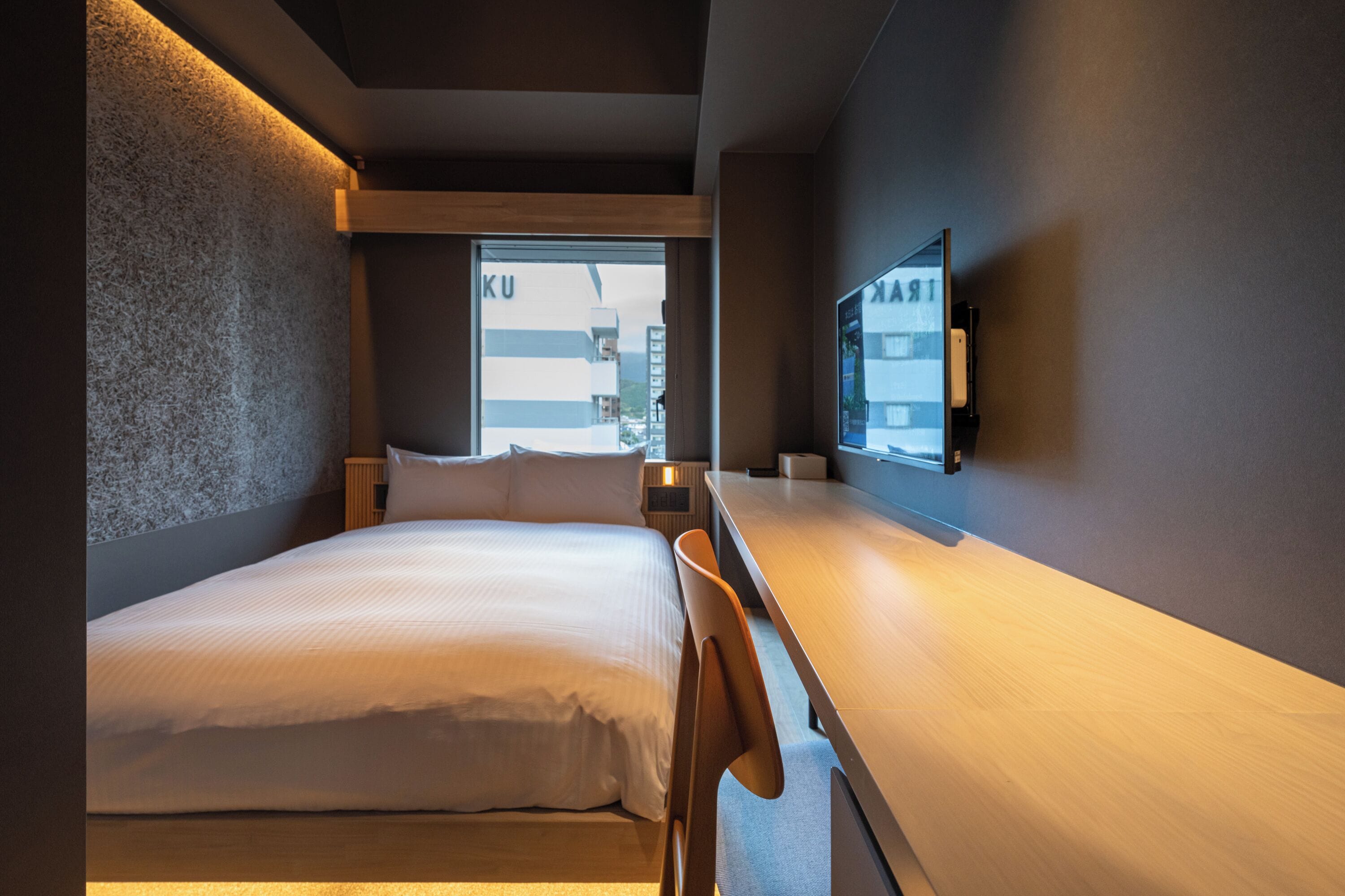 Quarto de hotel moderno com uma cama grande, uma escrivaninha e uma televisão fixada na parede.