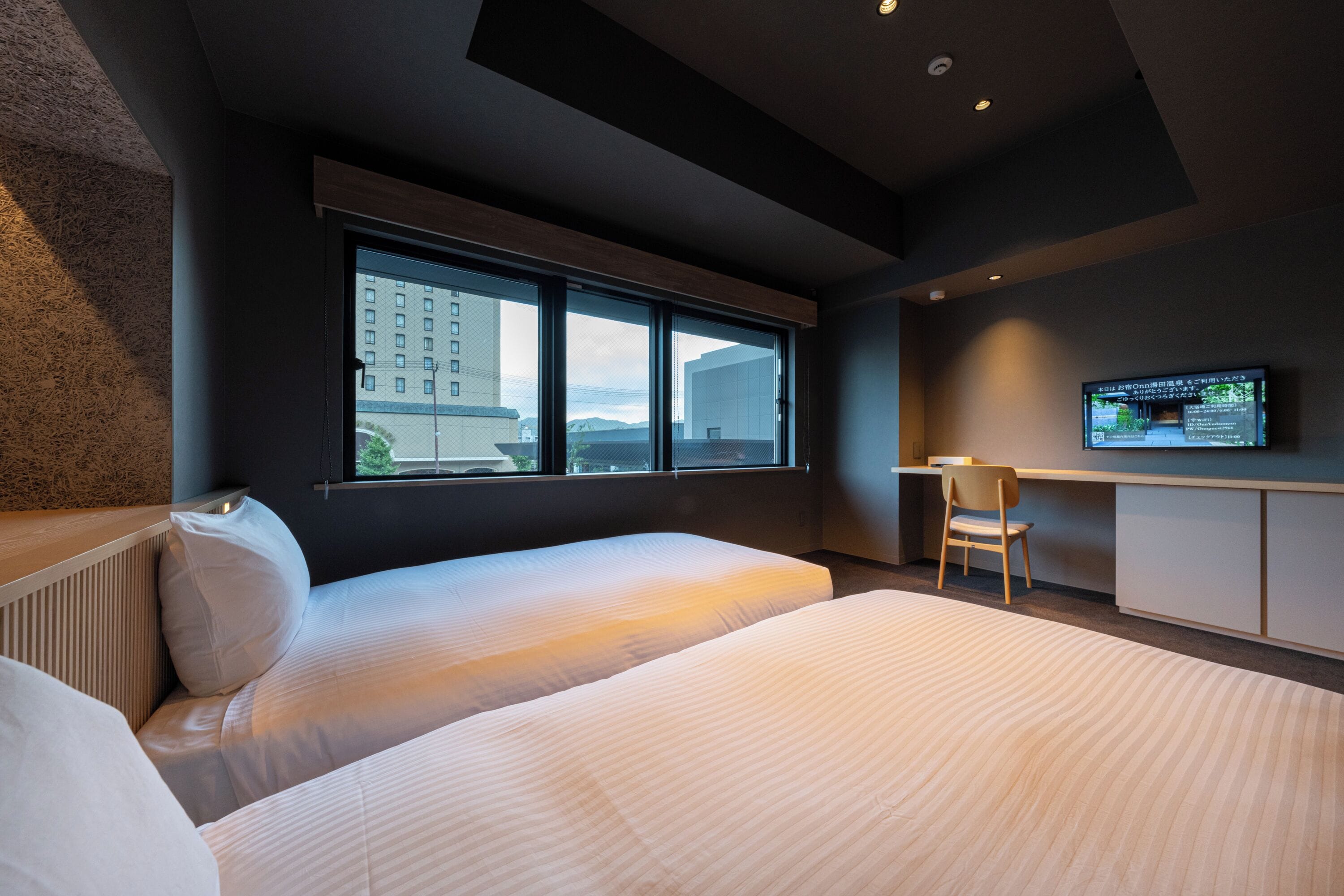 Une chambre d’hôtel moderne équipée de deux lits, d’une grande fenêtre, d’un bureau et d’une télévision.