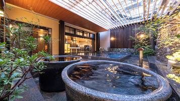 A modern outdoor area with a stone fountain, potted plants, and a wooden pergola.