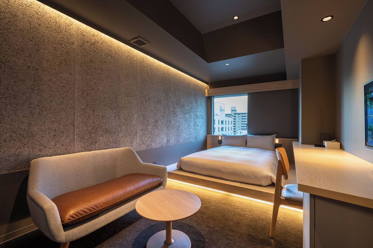 Habitación de hotel moderna con sofá, una mesita redonda, cama y vista a la ciudad a través de un ventanal grande.