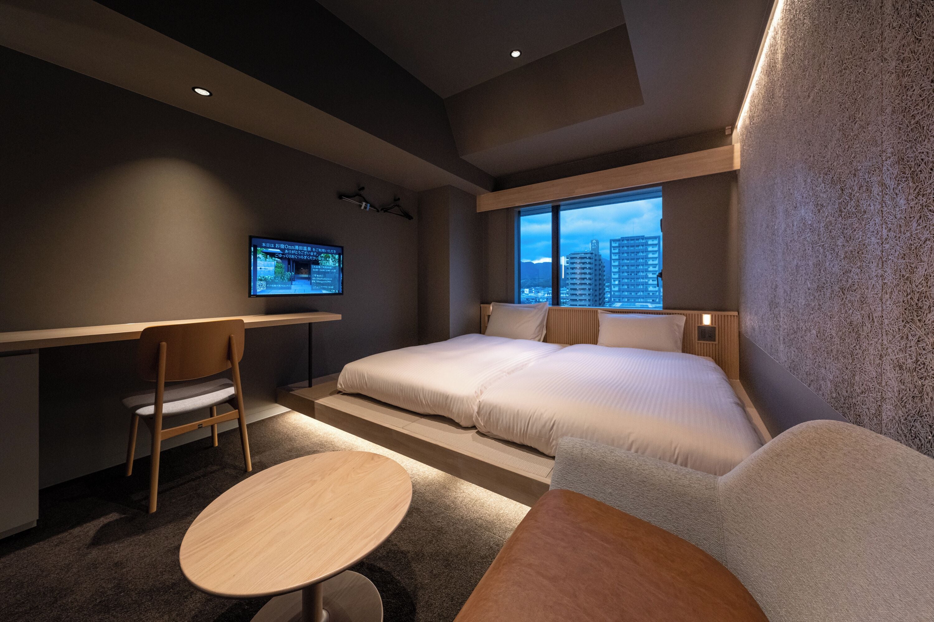 A modern hotel room with a large bed, a desk, a chair, and a TV.