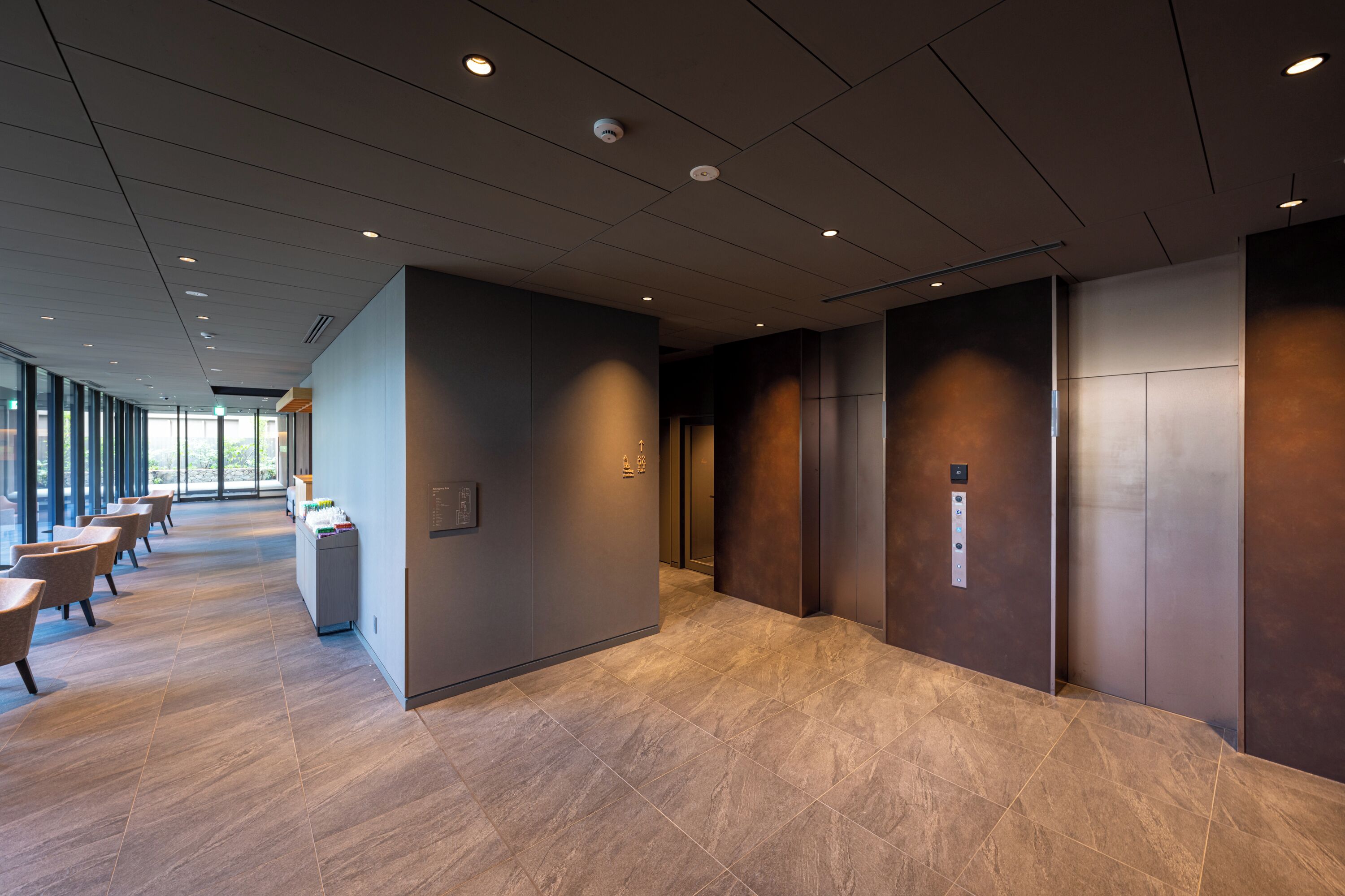 A modern hallway with a marble floor, a reception desk, and a set of elevators.