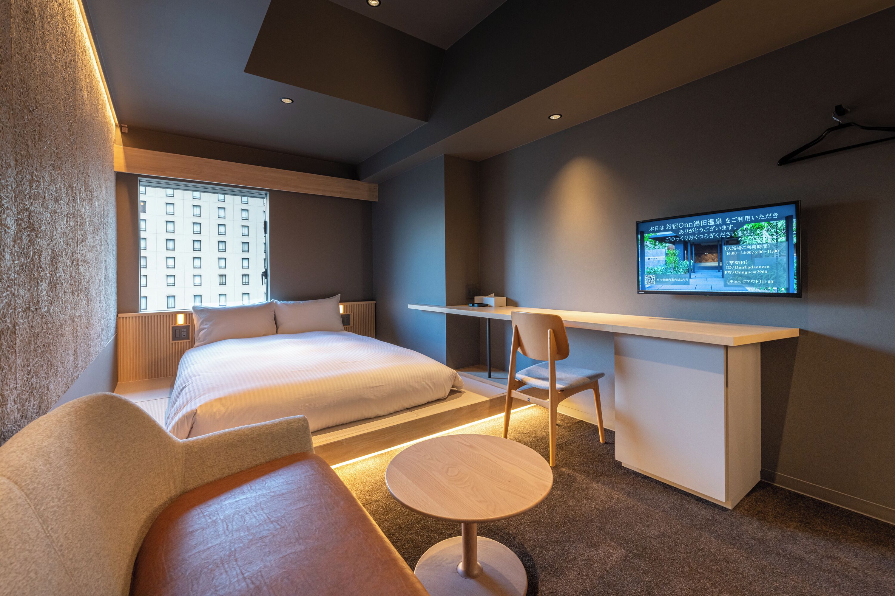 A modern hotel room with a large bed, a desk, a chair, and a television on the wall.