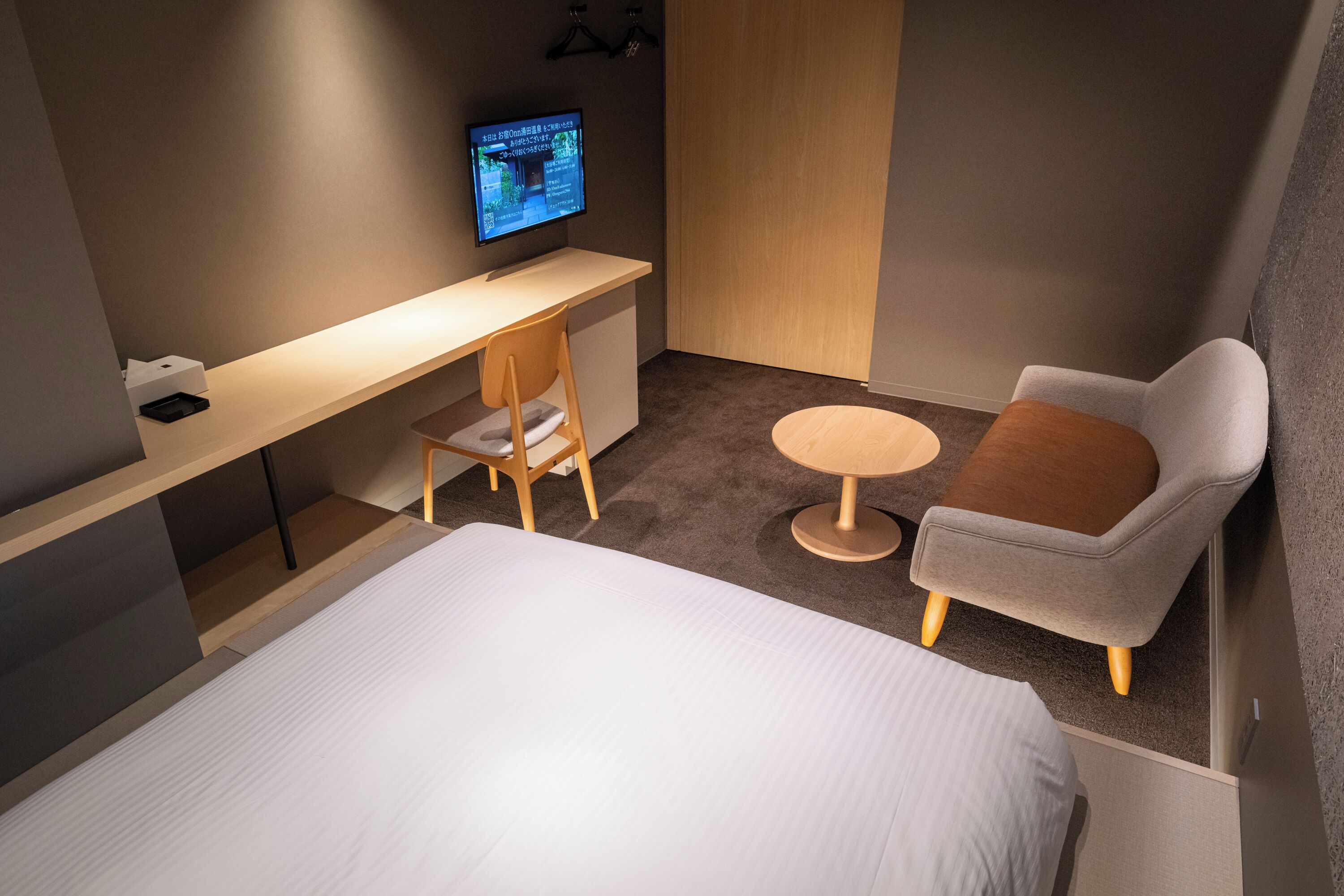 Habitación de hotel con cama, escritorio con computadora, silla y una pequeña mesa redonda.