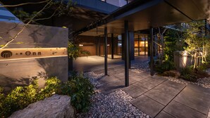 Una entrada de hotel moderna con fachada de piedra, zona de estar al aire libre y un corredor cubierto.