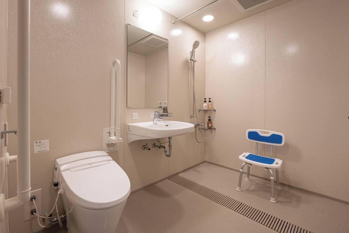 Un baño con inodoro, lavamanos, ducha y una pequeña silla azul y blanca.