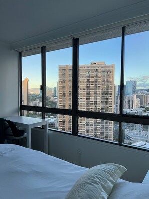 A hotel room with a large window, a bed, a desk, and a chair.