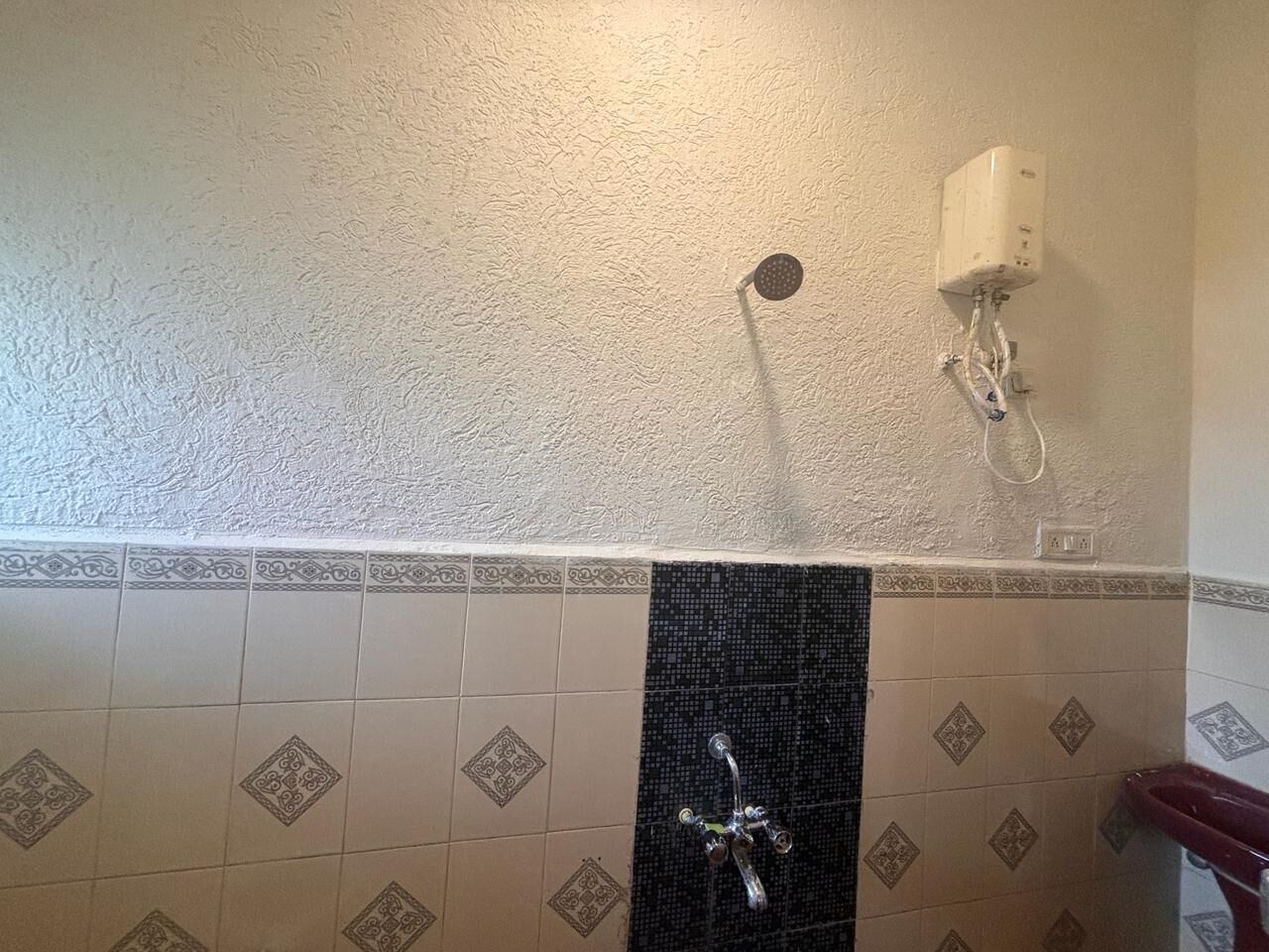 Un baño con ducha, pared blanca y azulejos estampados.