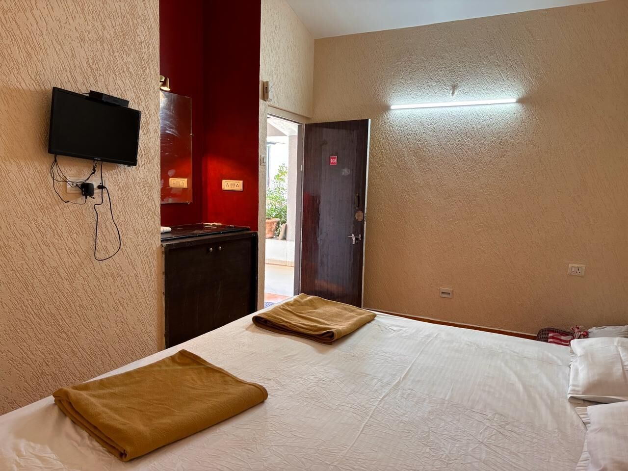 A hotel room with a bed, a television mounted on the wall, and a door leading to a balcony.