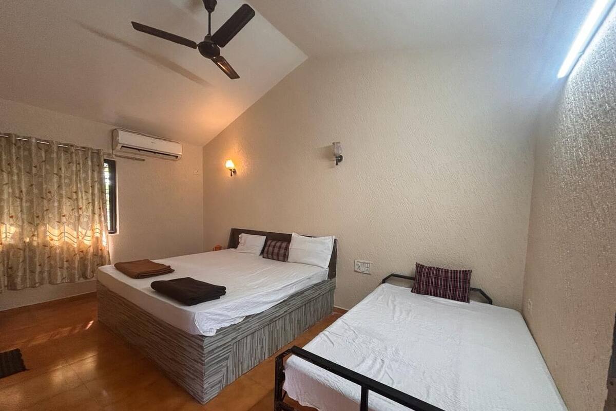 Habitación con dos camas, aire acondicionado, ventilador de techo y ventana con cortinas.