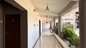 Un pasillo largo y estrecho con suelo de baldosas, paredes blancas y una puerta de madera a la izquierda.