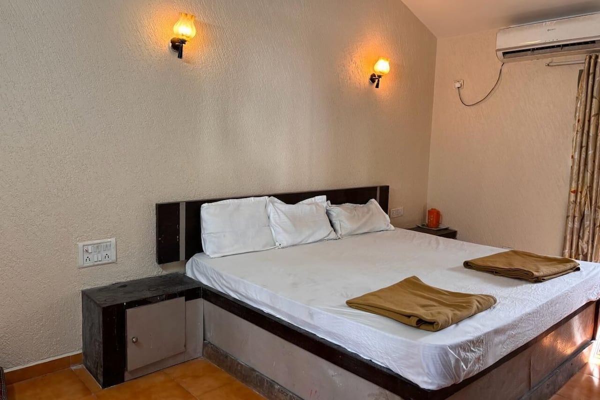 Habitación de hotel con cama, mesitas de noche, luces en la pared, un equipo de aire acondicionado y un enchufe.