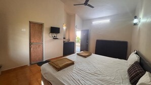 Habitación de hotel con cama, ventilador de techo, televisor de pantalla plana y puerta que da al exterior.