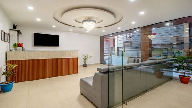 A modern reception area with a wooden reception desk, a flat-screen TV, and a seating area with a glass partition. - Treebo Shree Krishnam Residency (Thane)