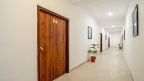 A hallway with wooden doors, numbered room signs, framed artwork on the walls, and potted plants. - Treebo Shree Krishnam Residency (Thane)