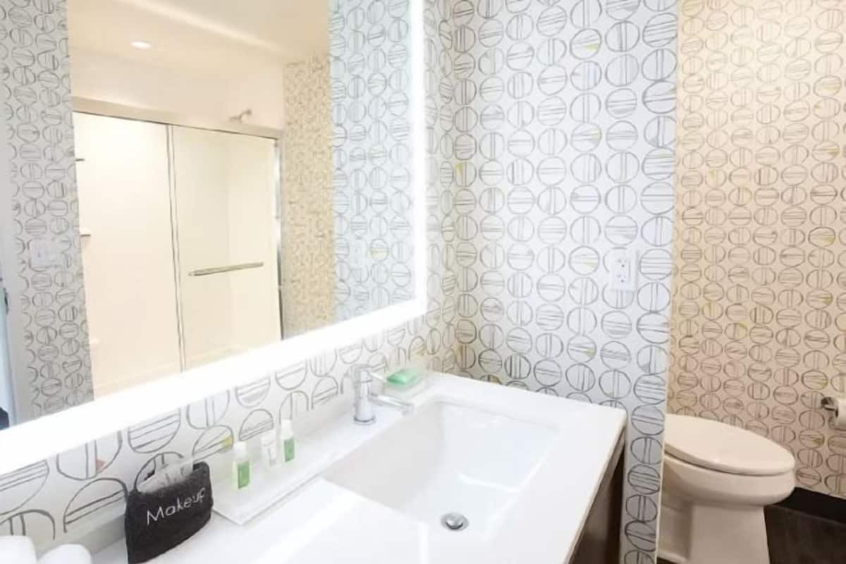 A bathroom with a white sink, a mirror, a toilet, and patterned wallpaper.