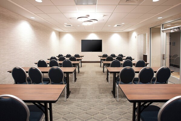 A conference room with a large flat-screen TV, multiple tables, and chairs arranged for meetings. - Holiday Inn Louisville Downtown (Louisville)
