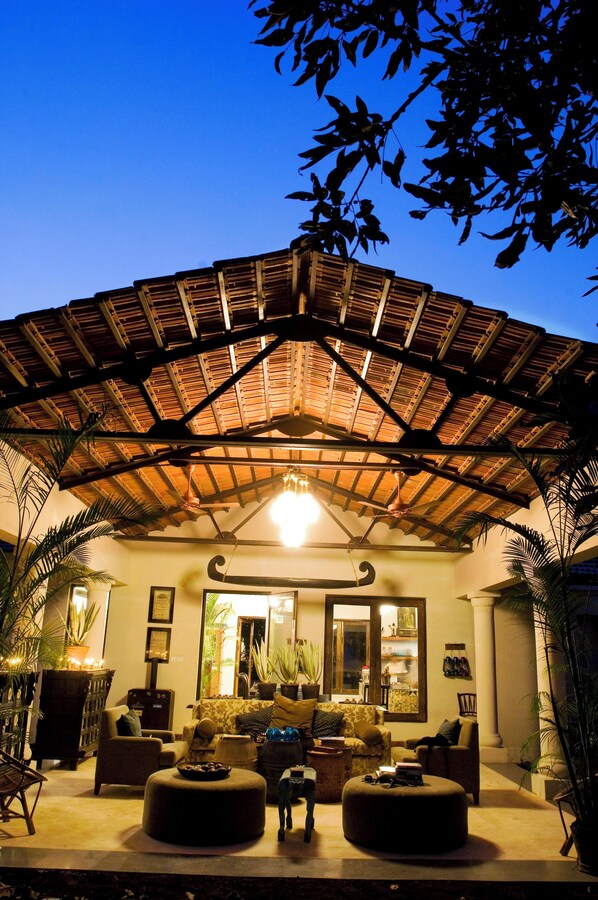 An indoor seating area with a thatched roof, cushioned seating, and potted plants. - Baghvan A Taj Safari Lodge - Pench National Park (Kurai)