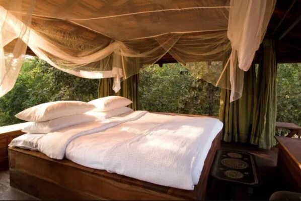 Una cama con sábanas blancas, cabecera de madera y cortinas traslúcidas.