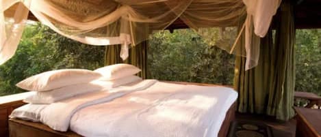 A bed with white linens, a wooden headboard, and sheer curtains.
