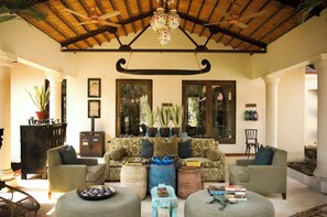 A spacious living area with a high ceiling, a sofa set, a fireplace, and a large window. - Baghvan A Taj Safari Lodge - Pench National Park (Kurai)