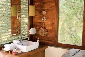 Ein Badezimmer mit Holzwand, einem großen Fenster, einem Waschbecken, einem Spiegel und einem Handtuchhalter.