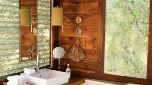 Un baño con pared de madera, un ventanal grande, un lavamanos, un espejo y un perchero para toallas.