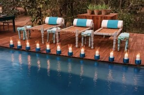 Uma área à beira da piscina com espreguiçadeiras de madeira e uma fileira de velas.