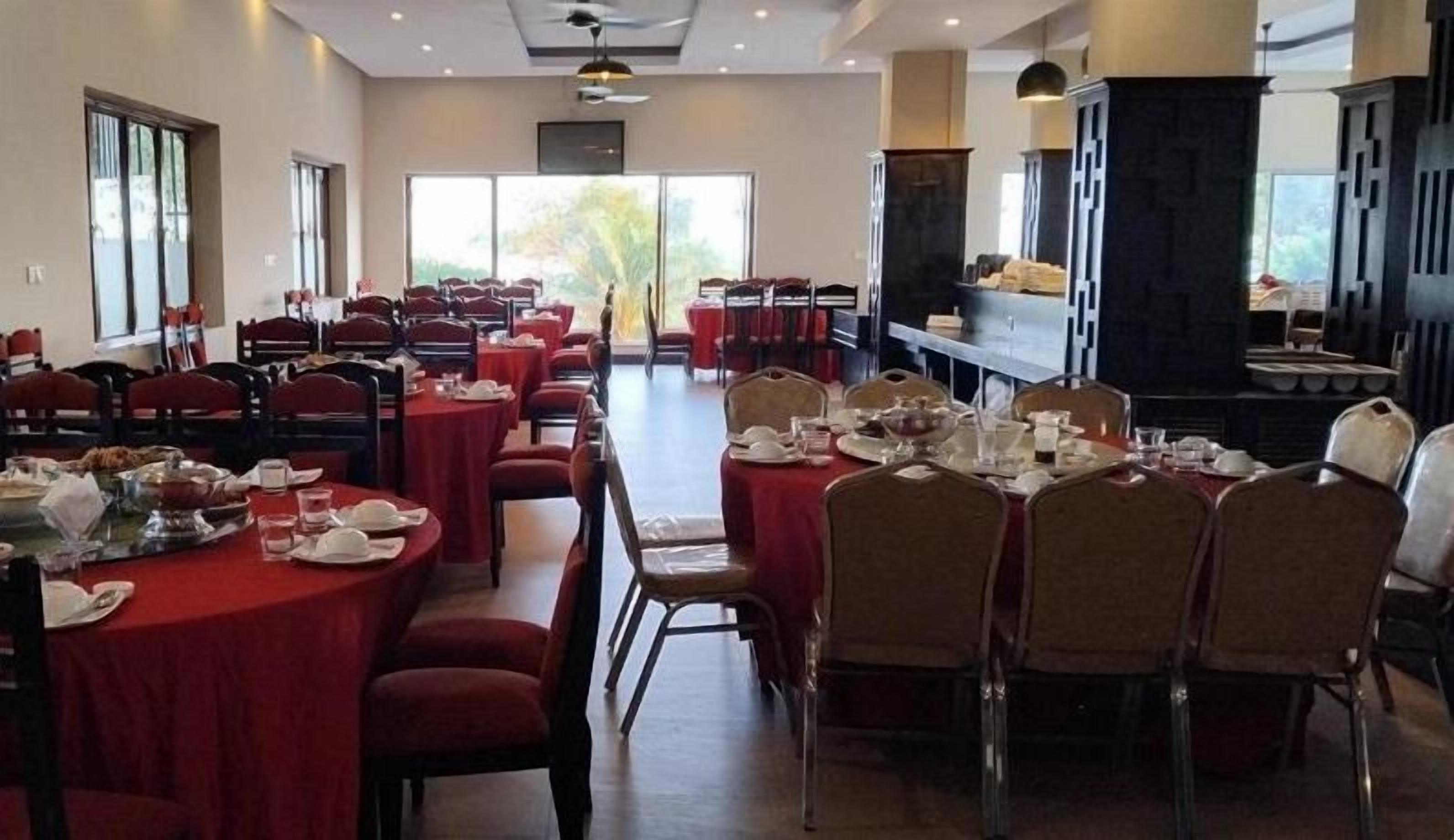 A dining area with round tables and chairs, a kitchen in the background, and large windows.