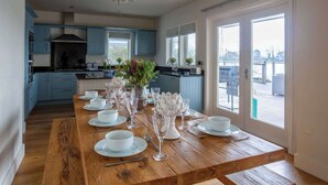 Una cocina moderna con armarios azules, una mesa de comedor de madera para seis personas y ventanas amplias que ofrecen vistas de la ciudad.