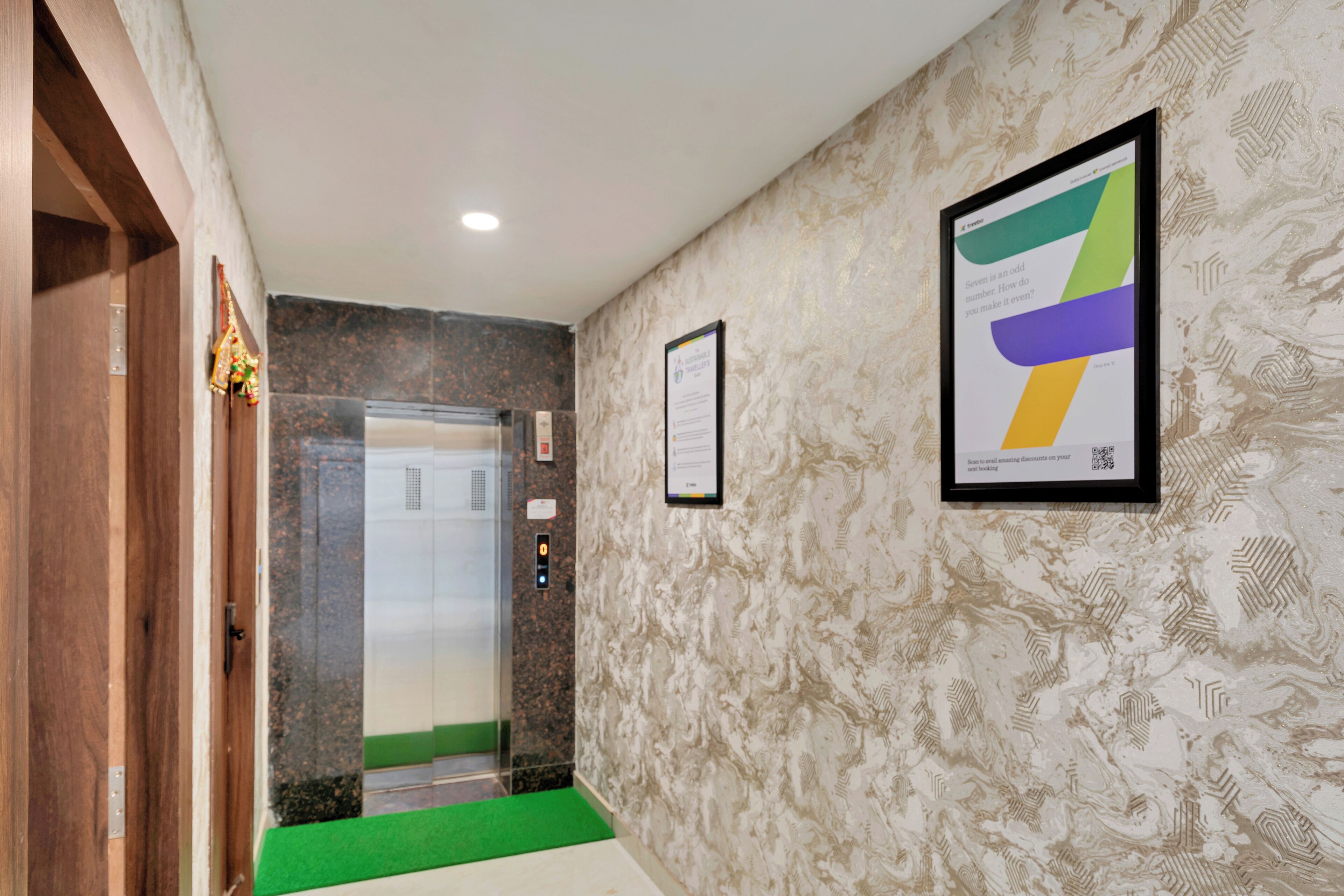 A hallway with a green carpet, a wooden door, an elevator, and a patterned wall with a framed certificate.