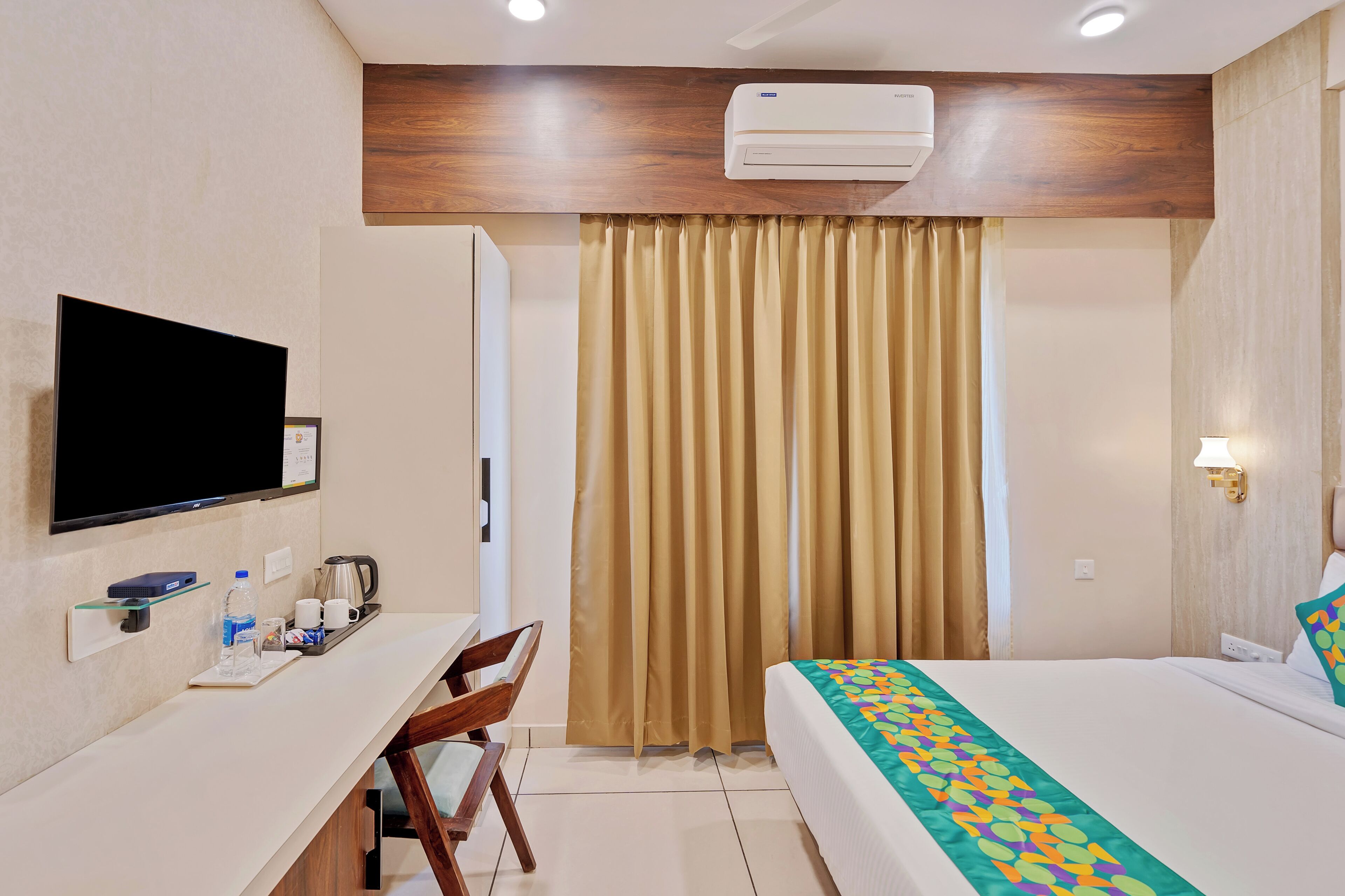 A hotel room with a bed, a desk, a chair, a television, an air conditioner, and curtains.