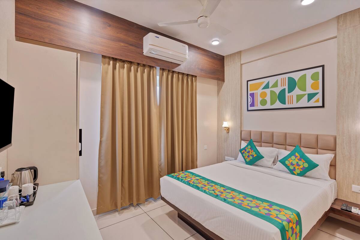 Una habitación de hotel con cama, escritorio, televisor, aire acondicionado y ventilador de techo.