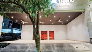 A hotel entrance with a tree in the foreground, a sign for 'treetbo Hotel Aura', and two red doors in the background. - Treebo The Aura (Bhubaneshwar)