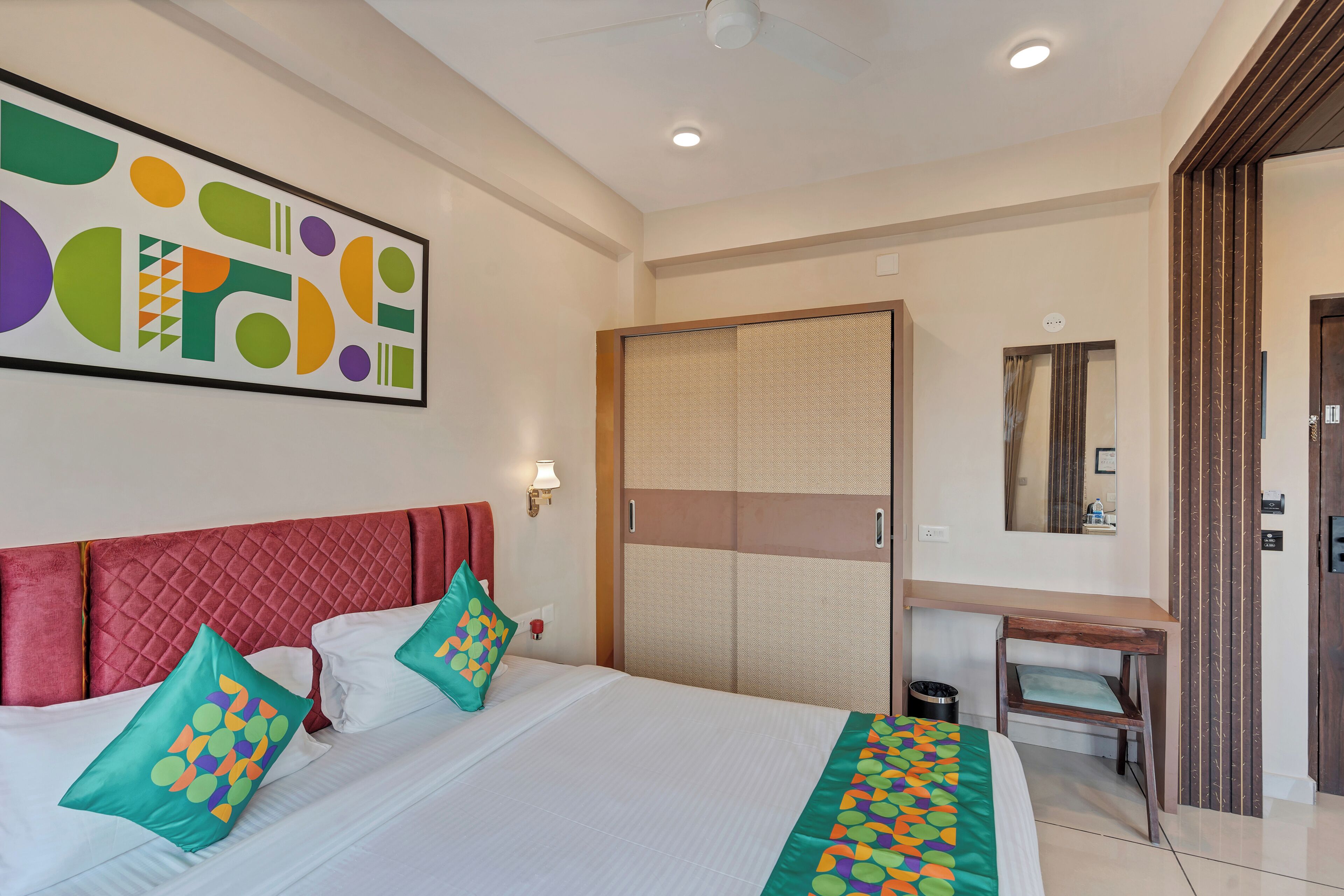 A hotel room with a bed, pillows, a desk, a mirror, and a wardrobe.