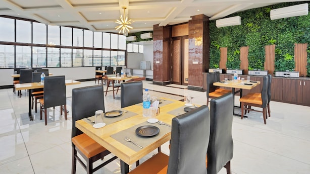 A modern dining area with tables, chairs, and a view of the cityscape through large windows. - Treebo The Aura (Bhubaneshwar)