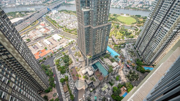 A high-rise building with a modern design, surrounded by a landscaped area with a swimming pool and a bridge in the background. - Landmark Condotel Art By KaySuite  (Ho Chi Minh City)