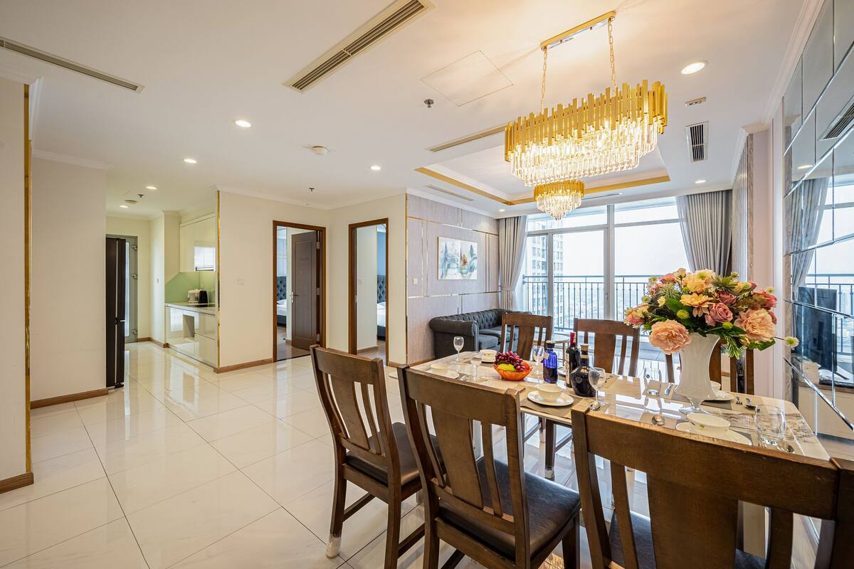 A dining area with a chandelier, a table set for four, and a vase of flowers.