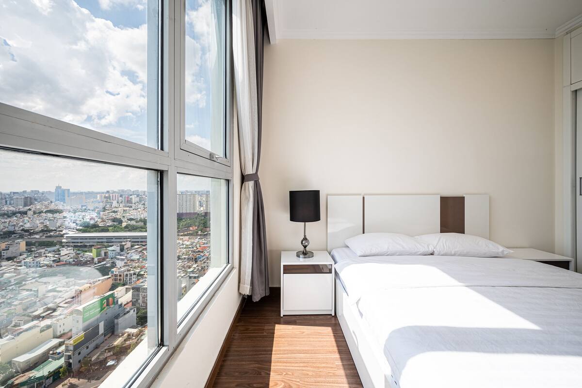 A modern hotel room with a large window, a bed, a nightstand, and a lamp.