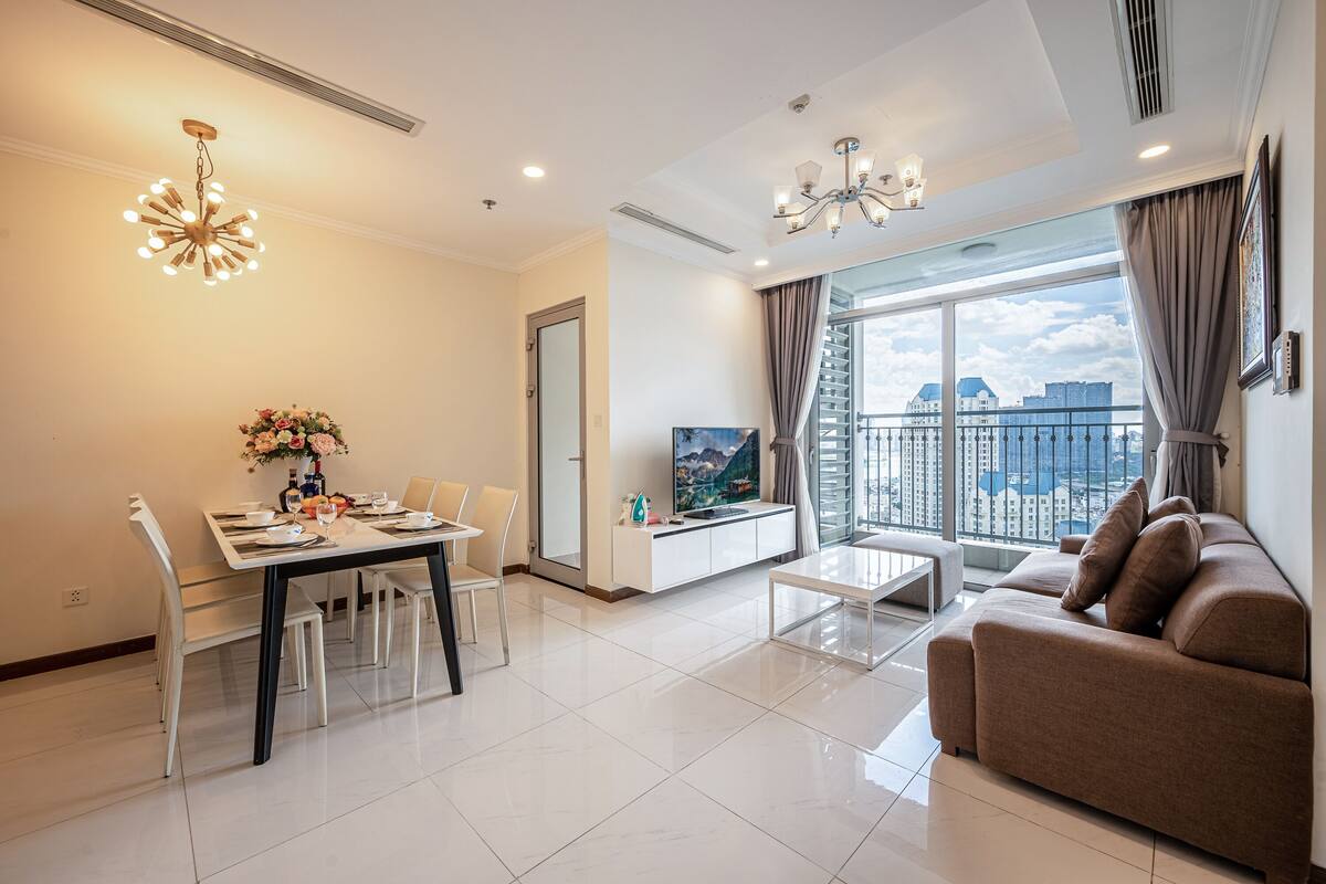 A modern living room with a dining area, a sofa, a TV, and a balcony with a city view.