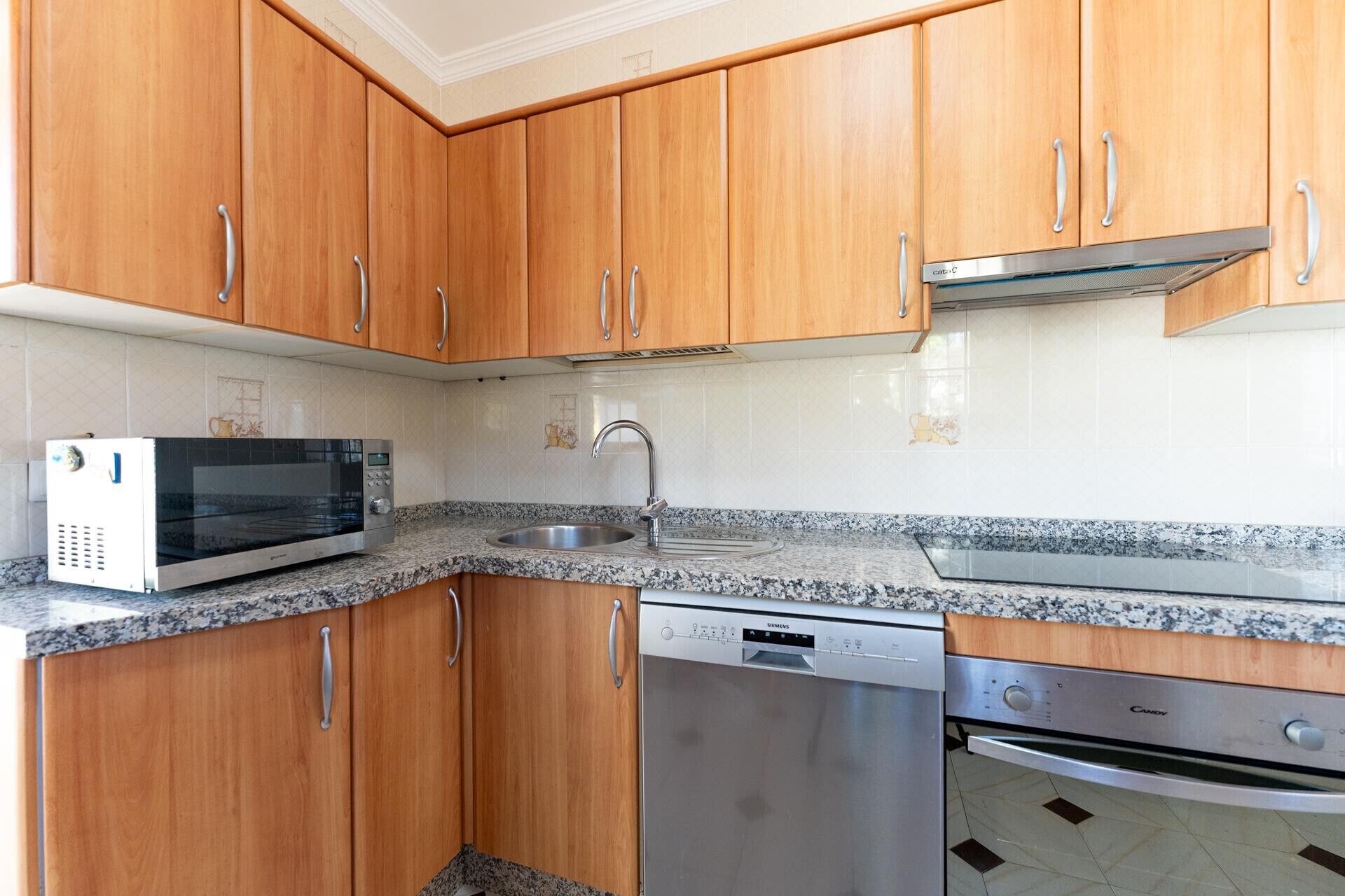 Una cocina con armarios de madera, microondas, lavaplatos, fregadero y estufa.