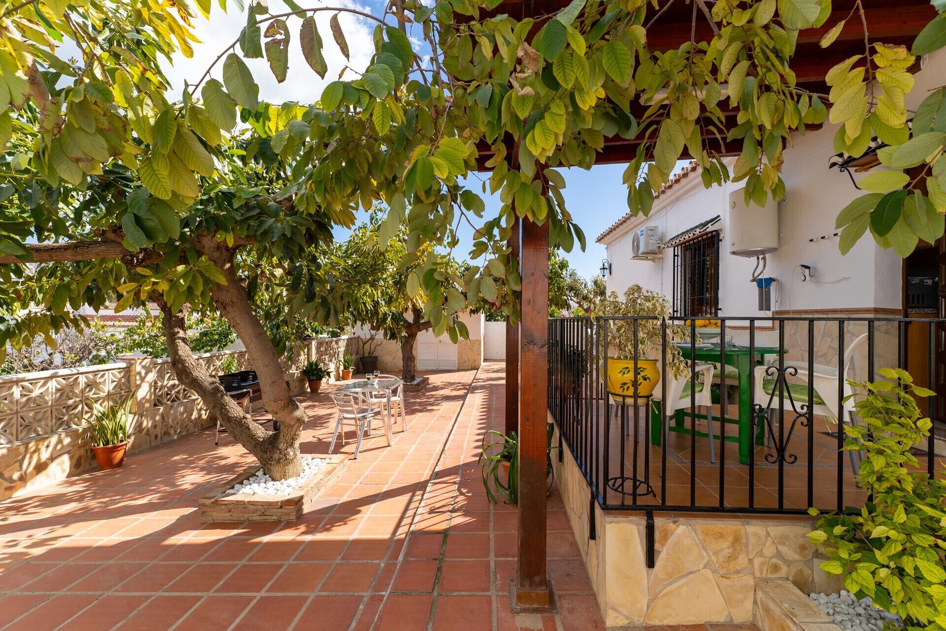 A patio with a table and chairs, surrounded by potted plants and a pergola.