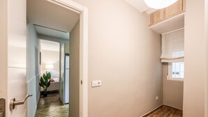 Un couloir avec un plancher en bois, une porte dotée d’une poignée et une fenêtre avec un store.