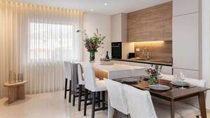 Una cucina moderna con un'isola centrale, una zona pranzo con tavolo apparecchiato per quattro e un'ampia finestra con tende leggere.