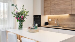 Una cucina moderna con un piano di lavoro bianco, mobili impiallacciati in legno, forno integrato e lavello in acciaio inossidabile.