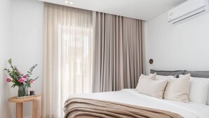 Una camera da letto moderna con un letto grande, un comodino con un vaso di fiori e una finestra con tende leggere.
