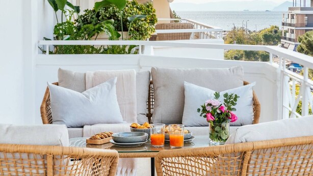 Un balcone con mobili in vimini, un tavolo con prodotti per la colazione e vista sul mare e sugli edifici.